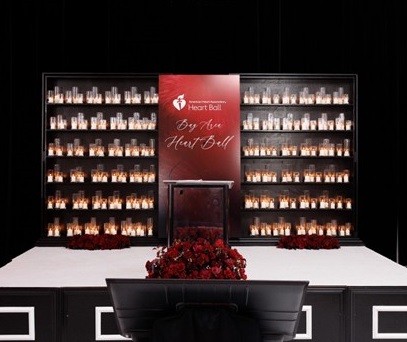 Empty stage with backdrop reading American Heart Association Bay Area Heart Ball between two walls of lit candles.